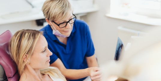 Zahnärztin erklärt Patientin im Zahnarztstuhl ein Röntgenbild