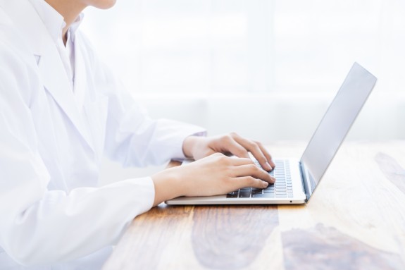 Person im Arztkittel sitzt am Laptop